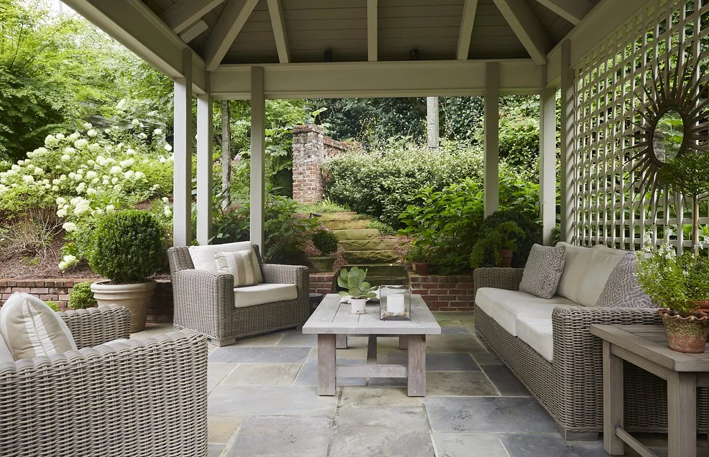 A view of inside of the terrace, with beautiful wicker seating & a coffee table, surrounded by vibrant greenery & flowers.