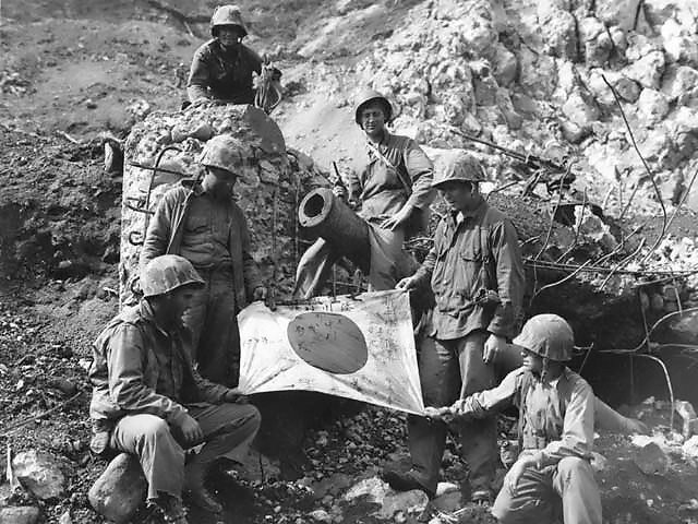 U.S. Marines pose with a captured Japanese flag on top of enemy pillbox.