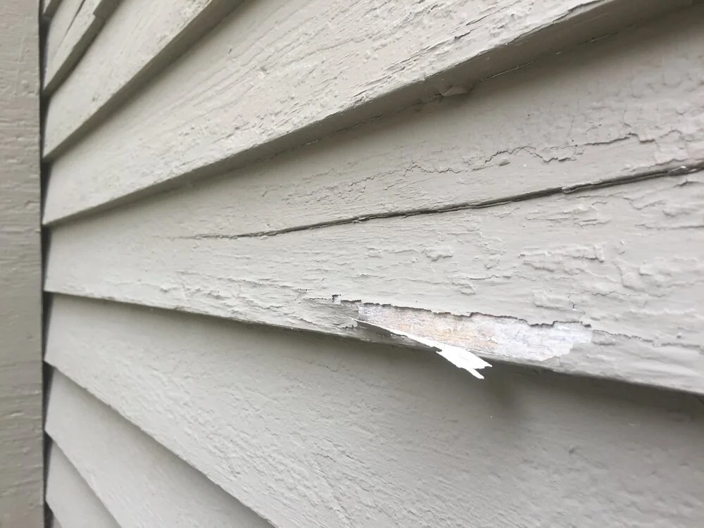 Chipped, peeling white paint on wooden clapboard siding