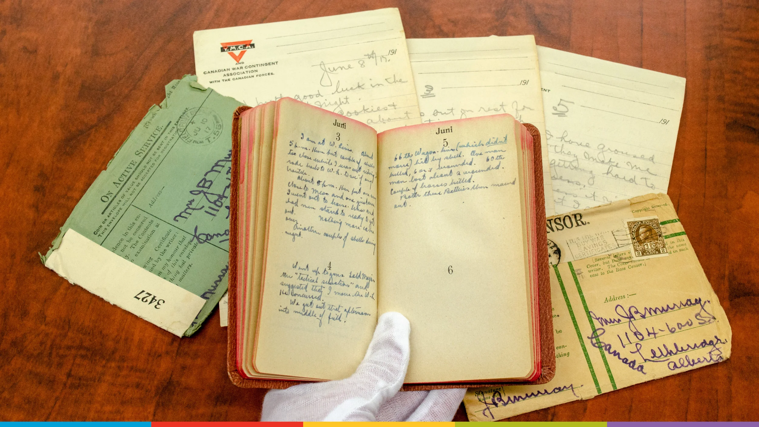 A photo of a gloved hand holding a journal from the Galt’s Archives with other archival documents behind.
