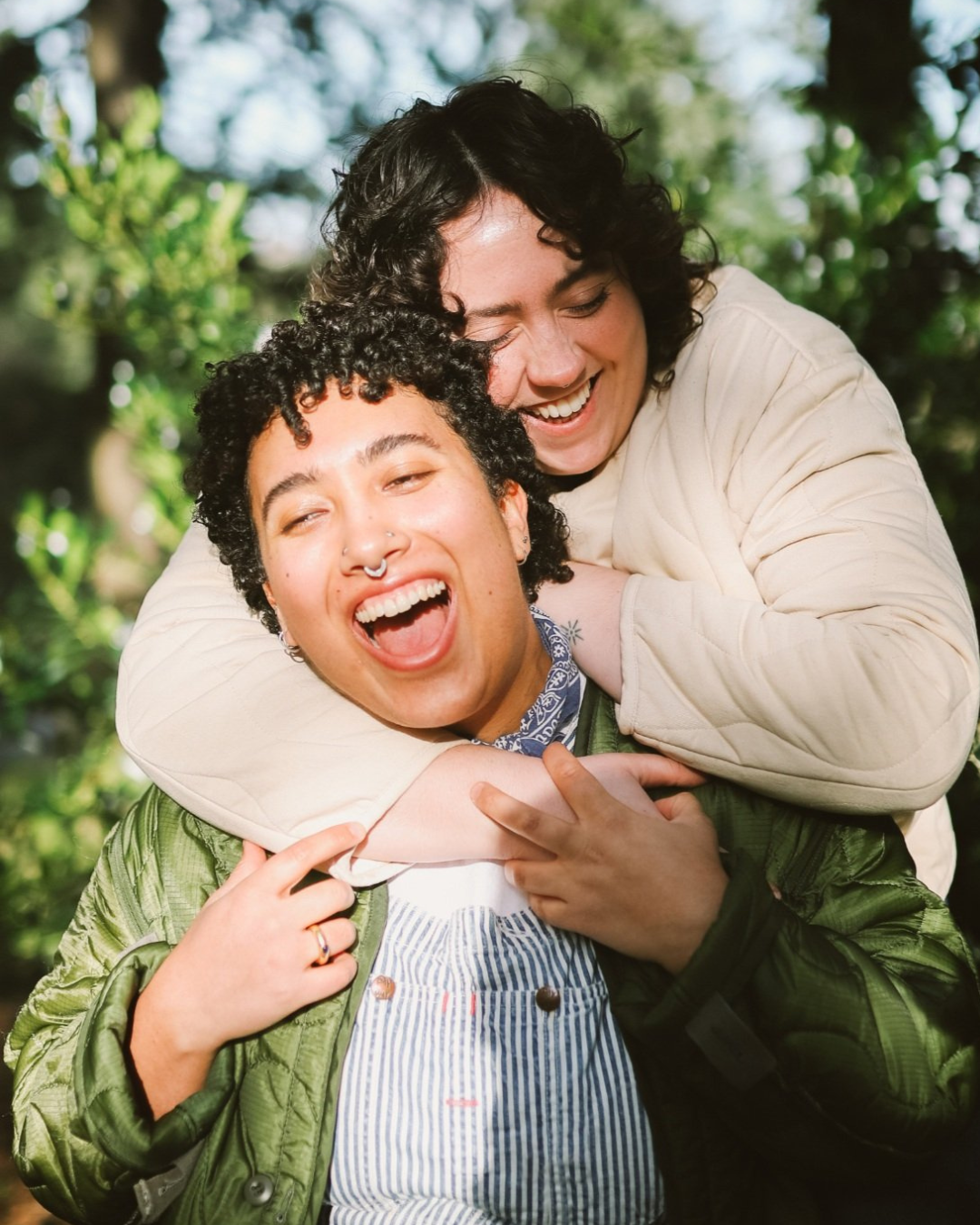 Two people are sharing a joyful hug outdoors surrounded by trees and greenery.