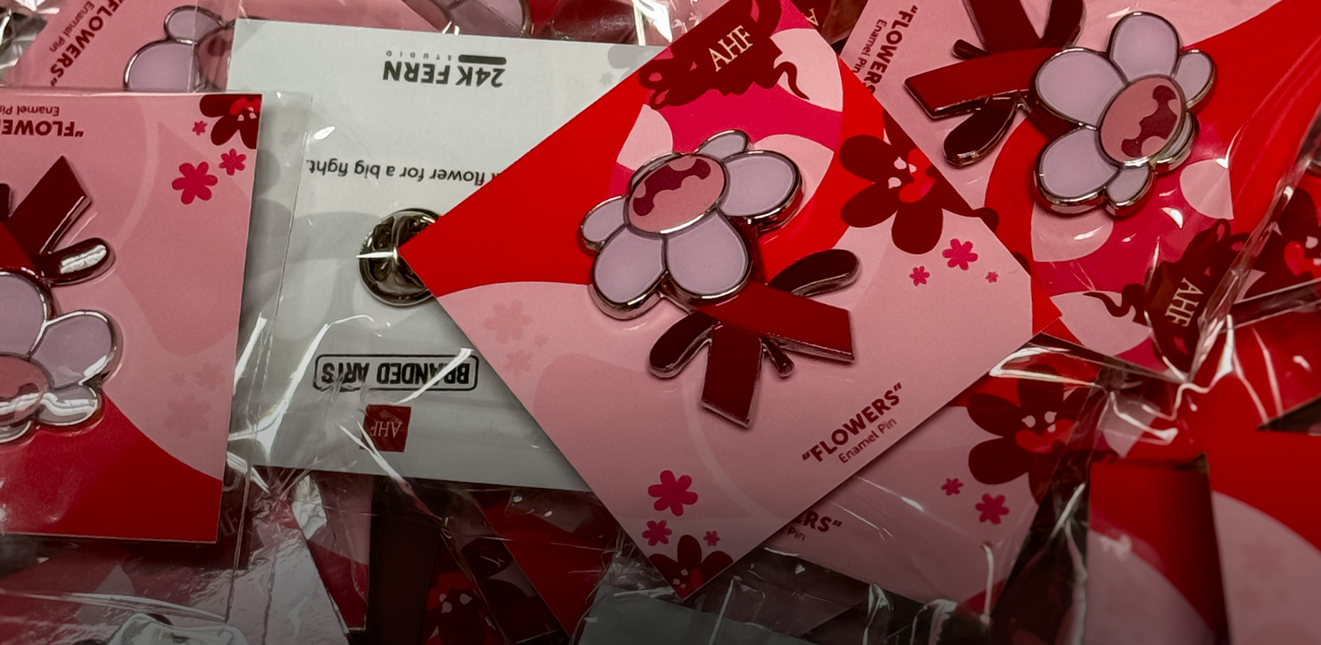 Pile of flower with a Red ribbon wrapped around the stem enamel pins on backing cards.