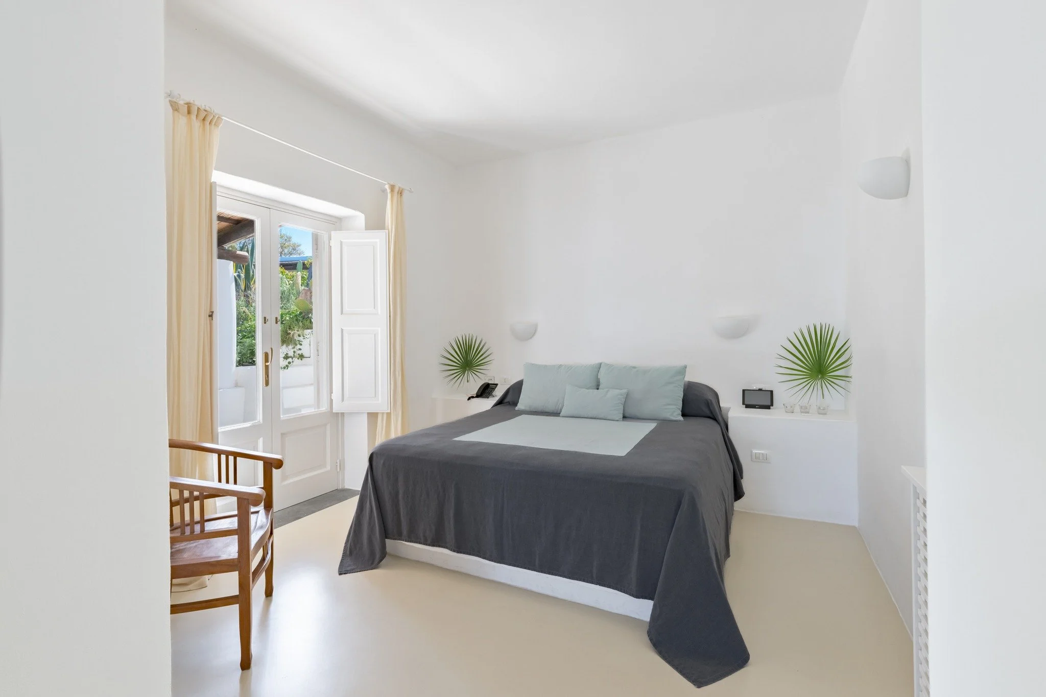 Spacious and inviting, the Junior Suites at Capofaro Resort welcome guests into an intimate setting where natural light softly filters, harmoniously blending the delicate tones of furnishings with the shimmering sea on the horizon and blooming flower