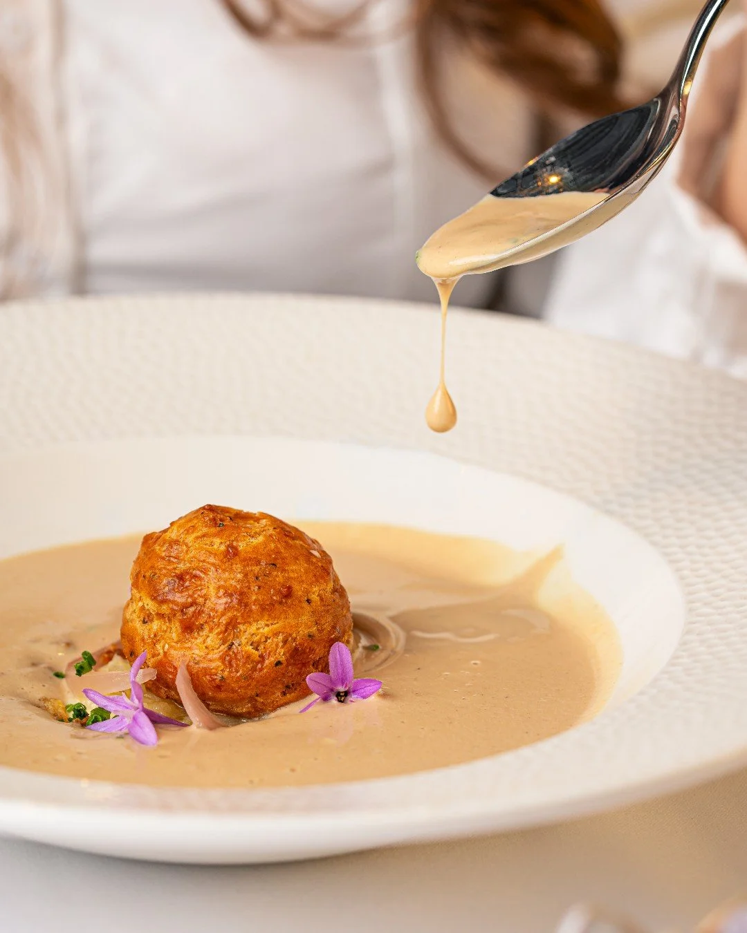 At the centre of the plate, a golden goug&egrave;re waits.

Then the malted cauliflower velout&eacute; cascades gently around the aged Comt&eacute;, steam rising softly as it meets sweet soubise onion and silky Mornay. Textures shift, flavours deepen