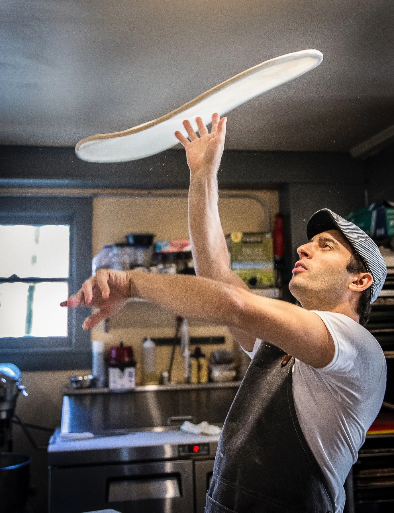 A man wearing a striped hat and black apron is impressively throwing pizza dough in the air