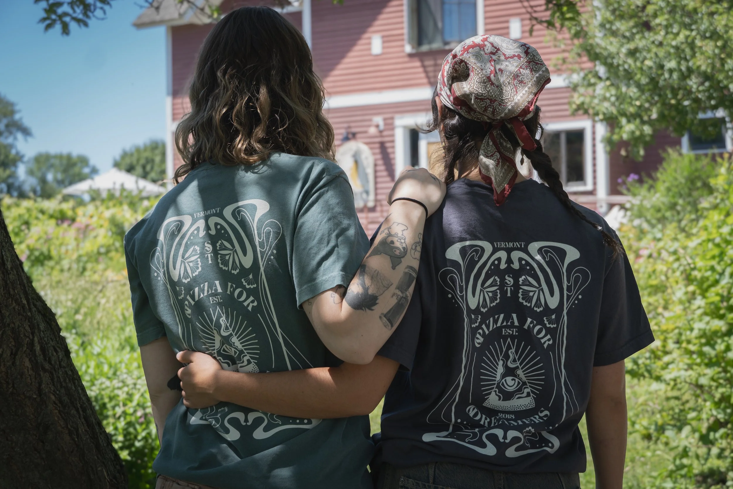 Two people standing outdoors near a tree, with their arms around each other, wearing matching t-shirts that say 'Vermont Quilts for Comfort.'