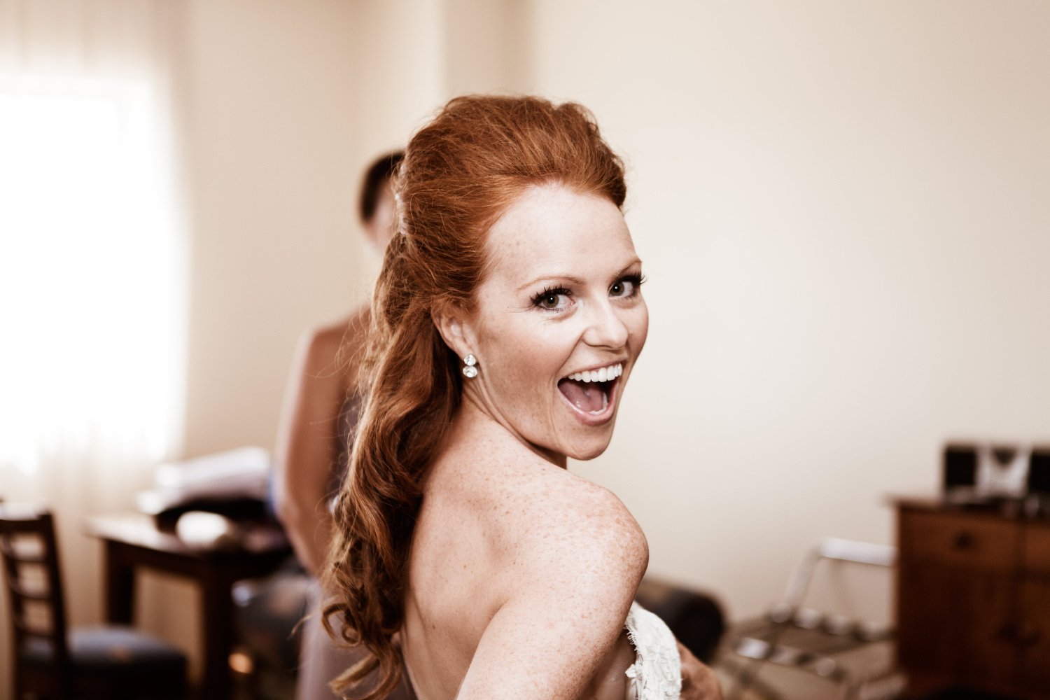 Smiling woman with red hair, wearing earrings, in a room with furniture.