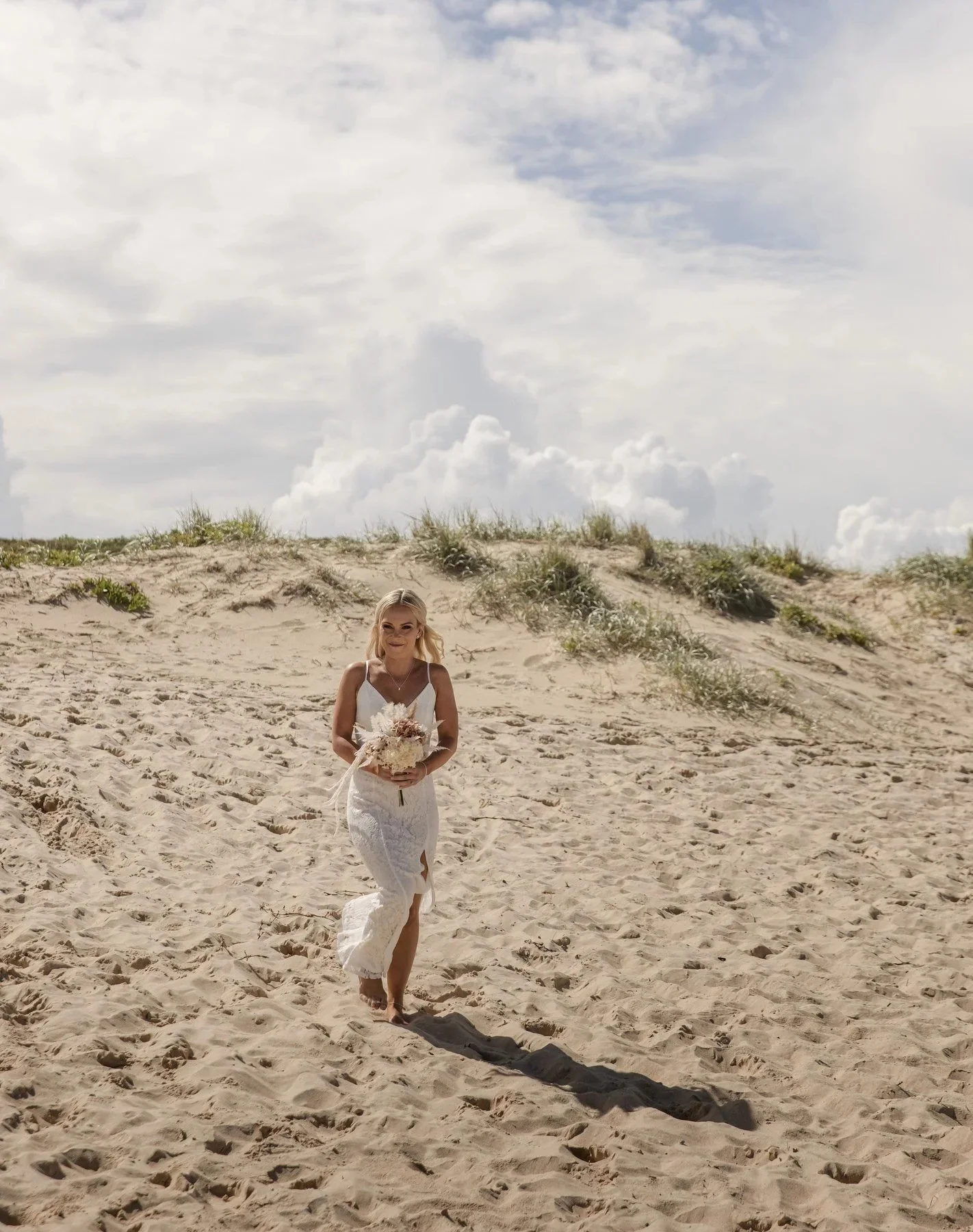 Bride walking across the sand dunes under a bright summer sky