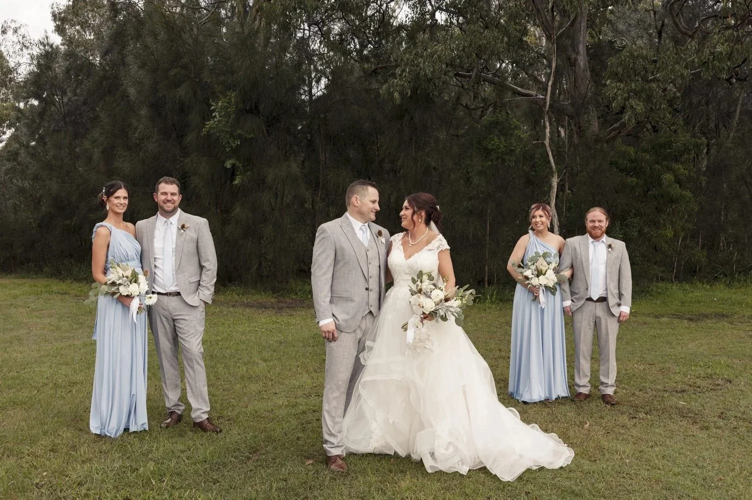 Bridal party portraits on the grass by the lake with bridesmaids in pale blue