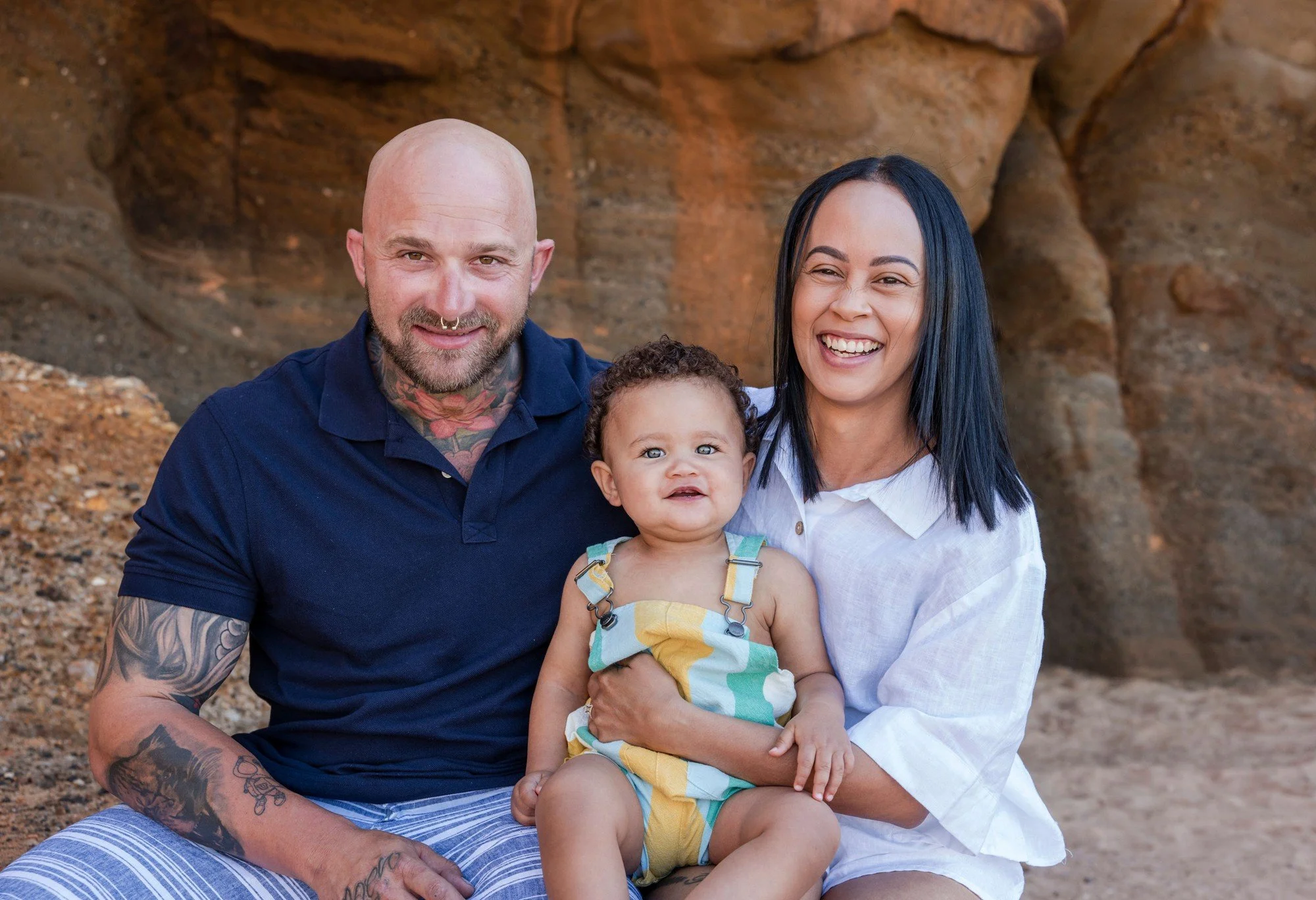 Parents laughing together with their baby against warm sandstone rocks