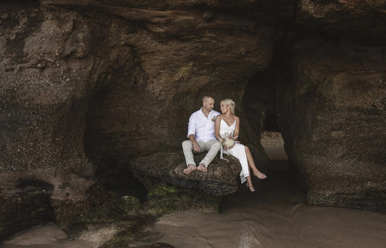 Couple and family seated on sandstone rocks at the mouth of a sea cave at Caves Beach