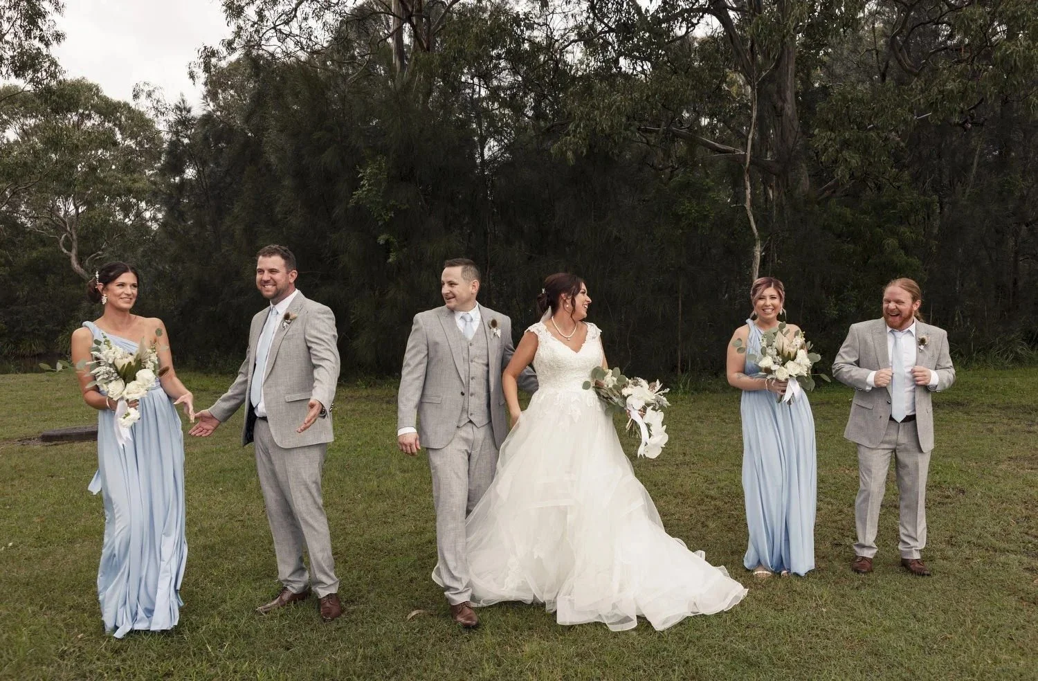 Bridal party walking and laughing across the lawn under the trees