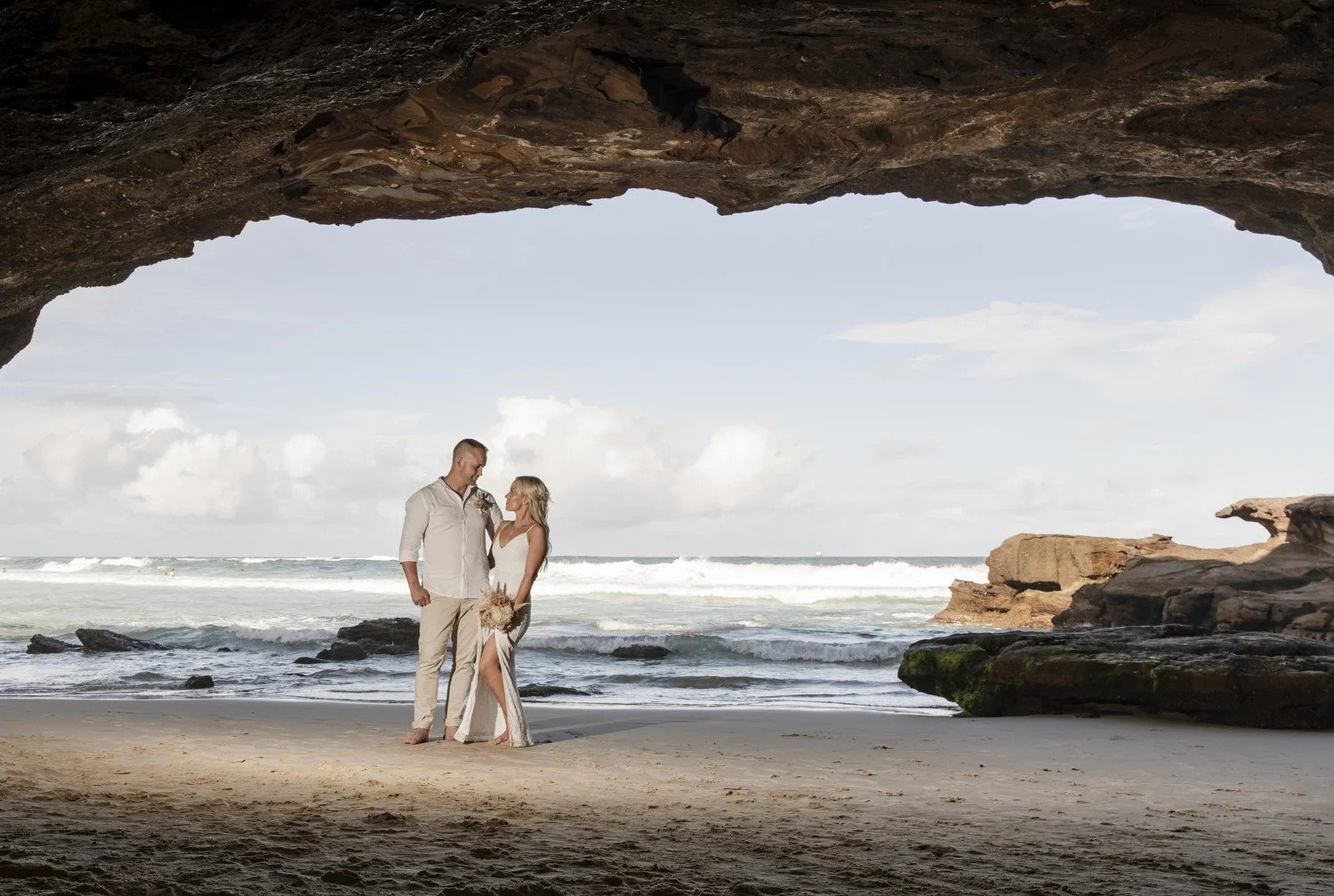 Couple framed by the arch of a sea cave with the ocean beyond
