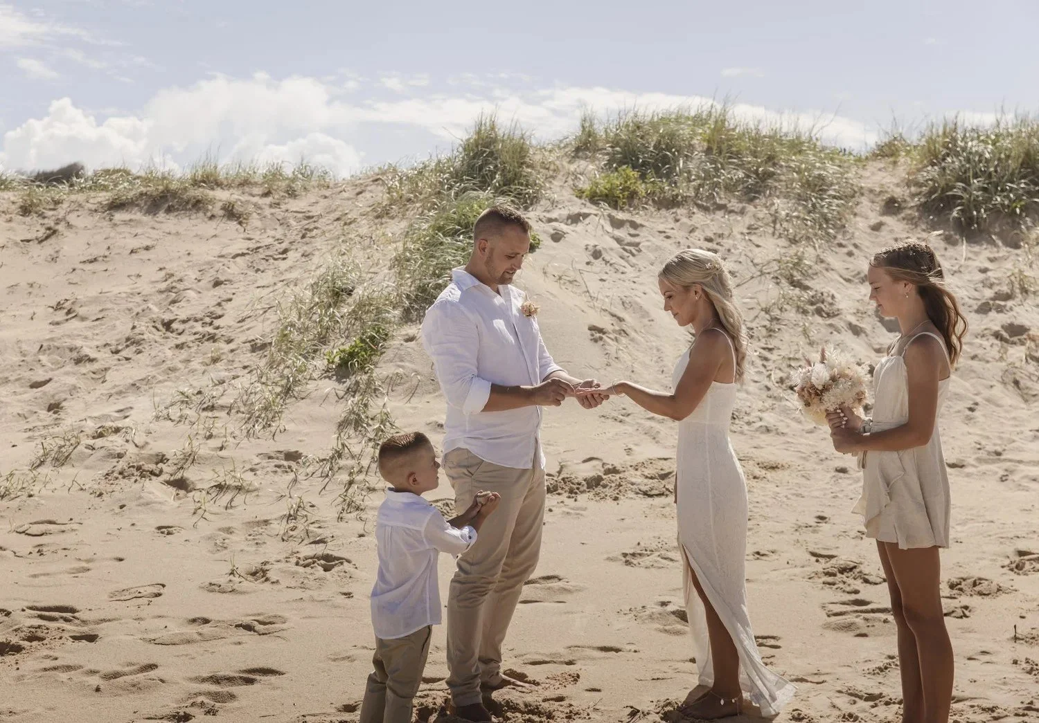 Couple holding hands with family beside them on the dunes at Caves Beach