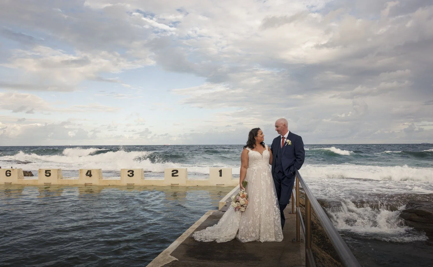 Bride and groom on an ocean-baths walkway with surf breaking behind them
