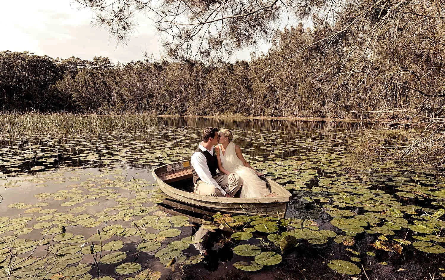 Relaxed newlyweds in a rowboat surrounded by water lilies
