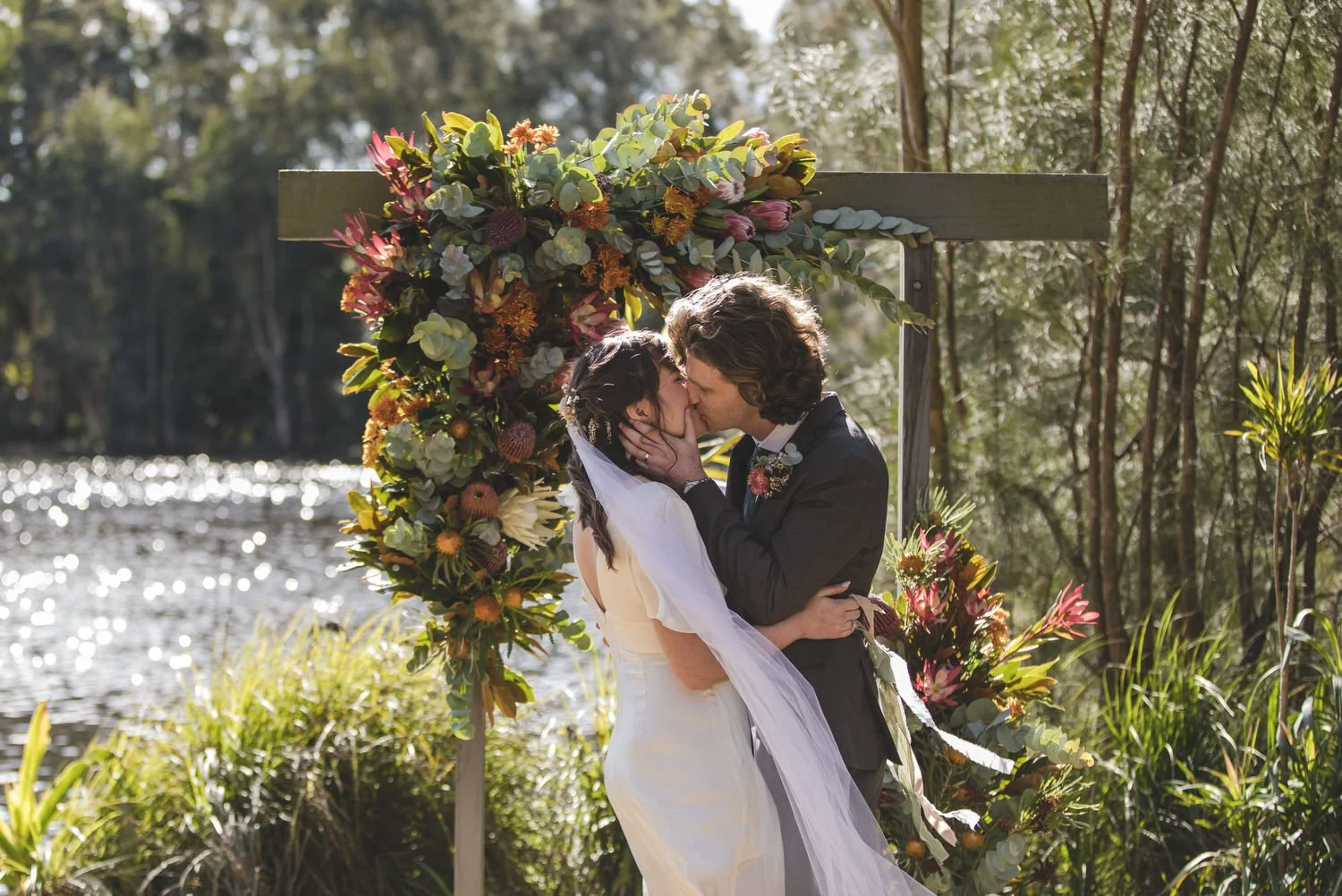 First kiss beside a native floral arbour by the lake at a Newcastle wedding