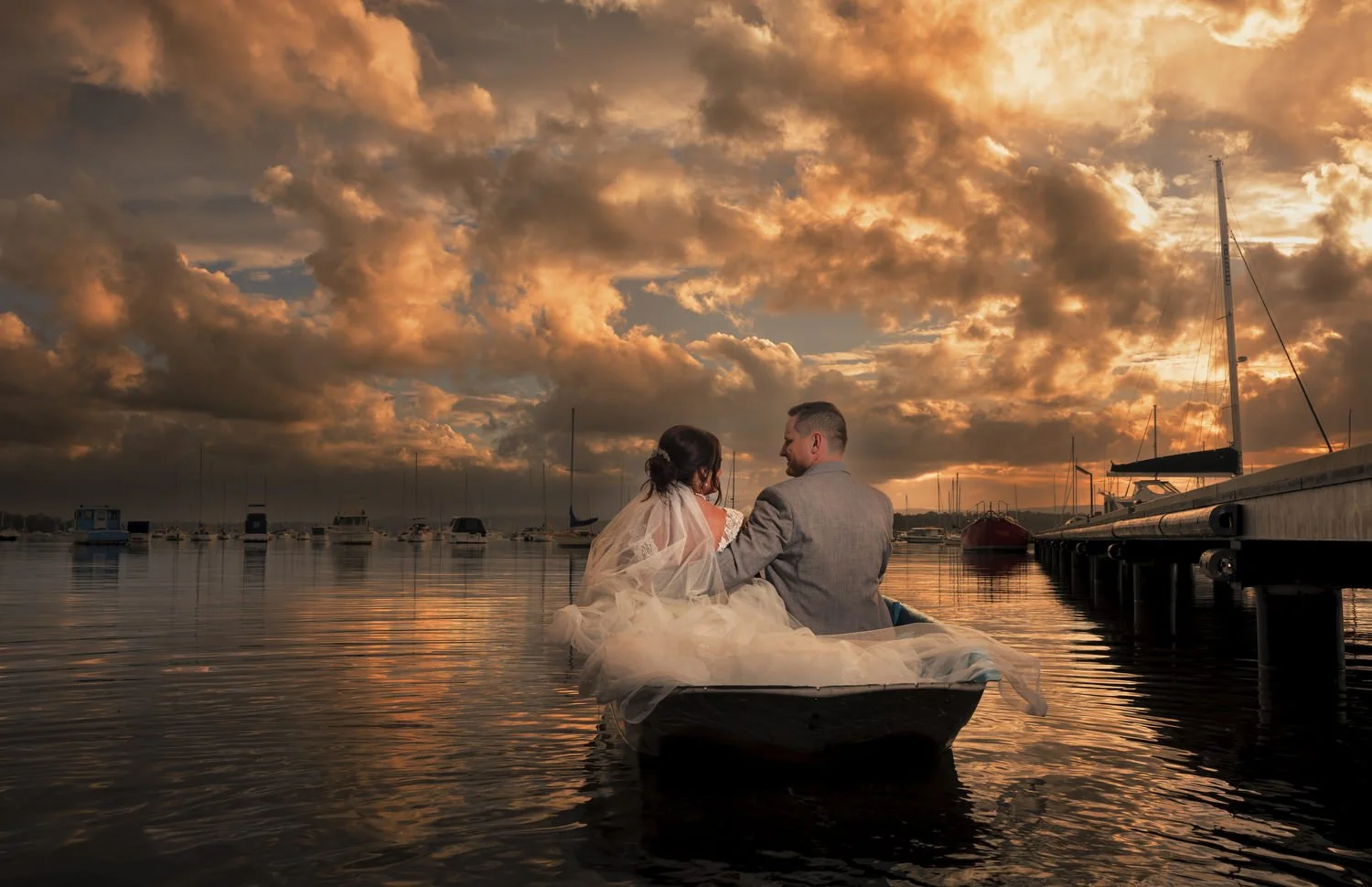 Bride and groom in a rowboat on glassy water under a blazing Lake Macquarie sunset