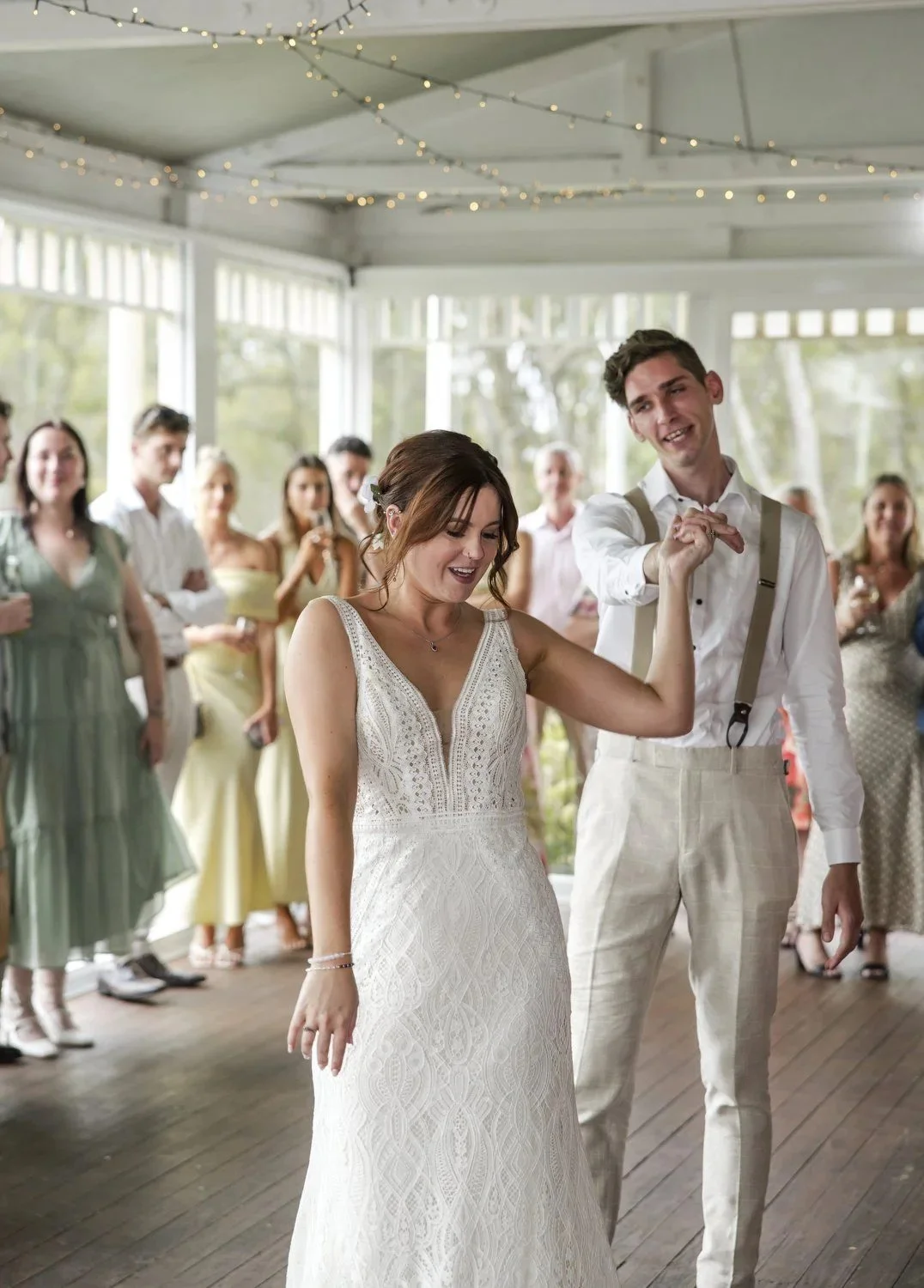 A groom twirling his bride during their first dance as guests watch and smile