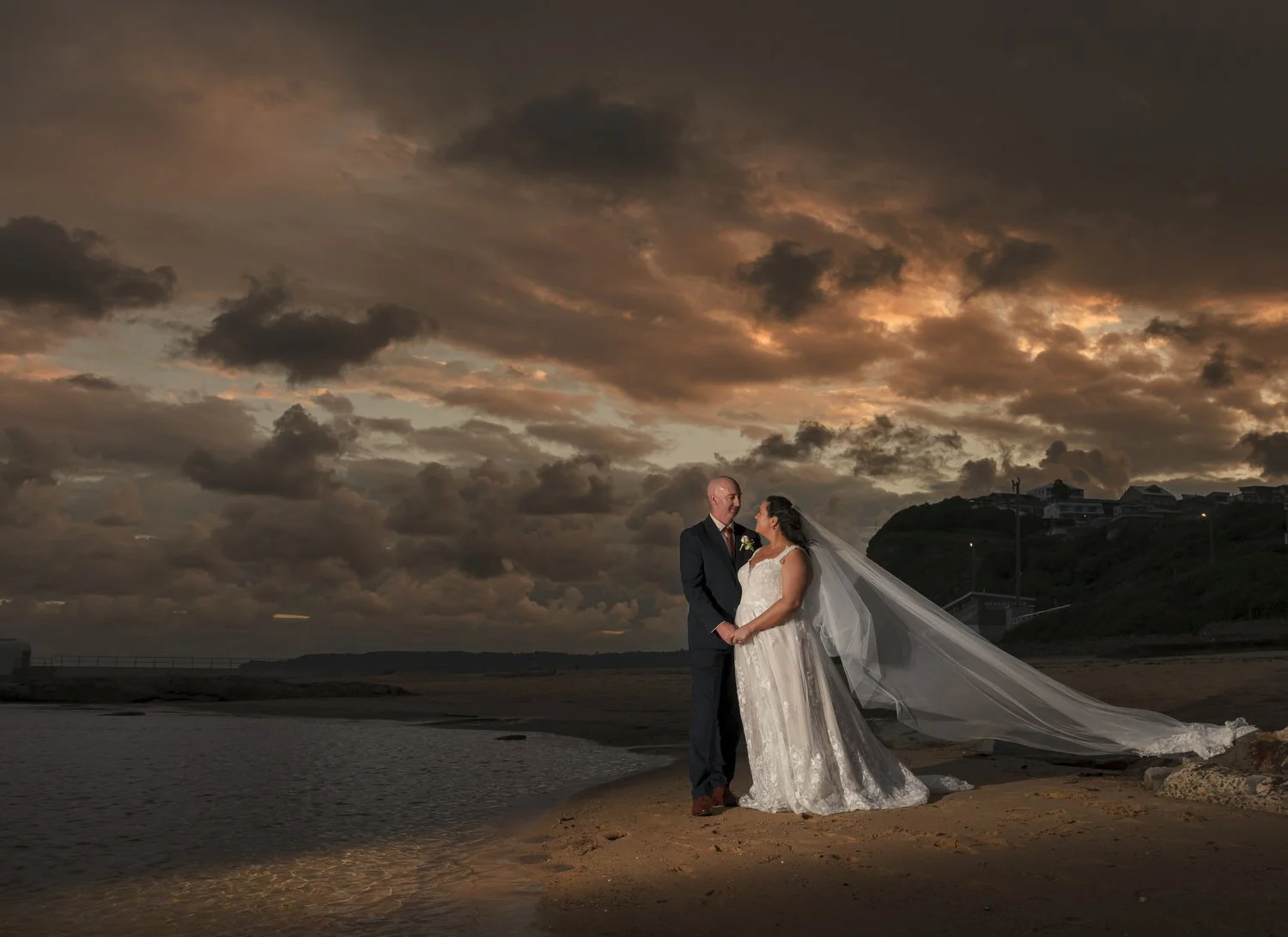 Couple and flying veil beneath a stormy dusk sky by the water