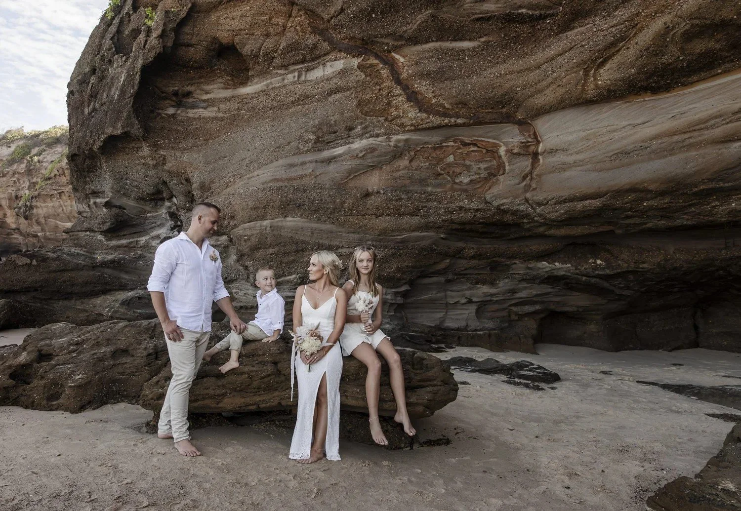 Couple and family seated on sandstone rocks at the mouth of a sea cave at Caves Beach