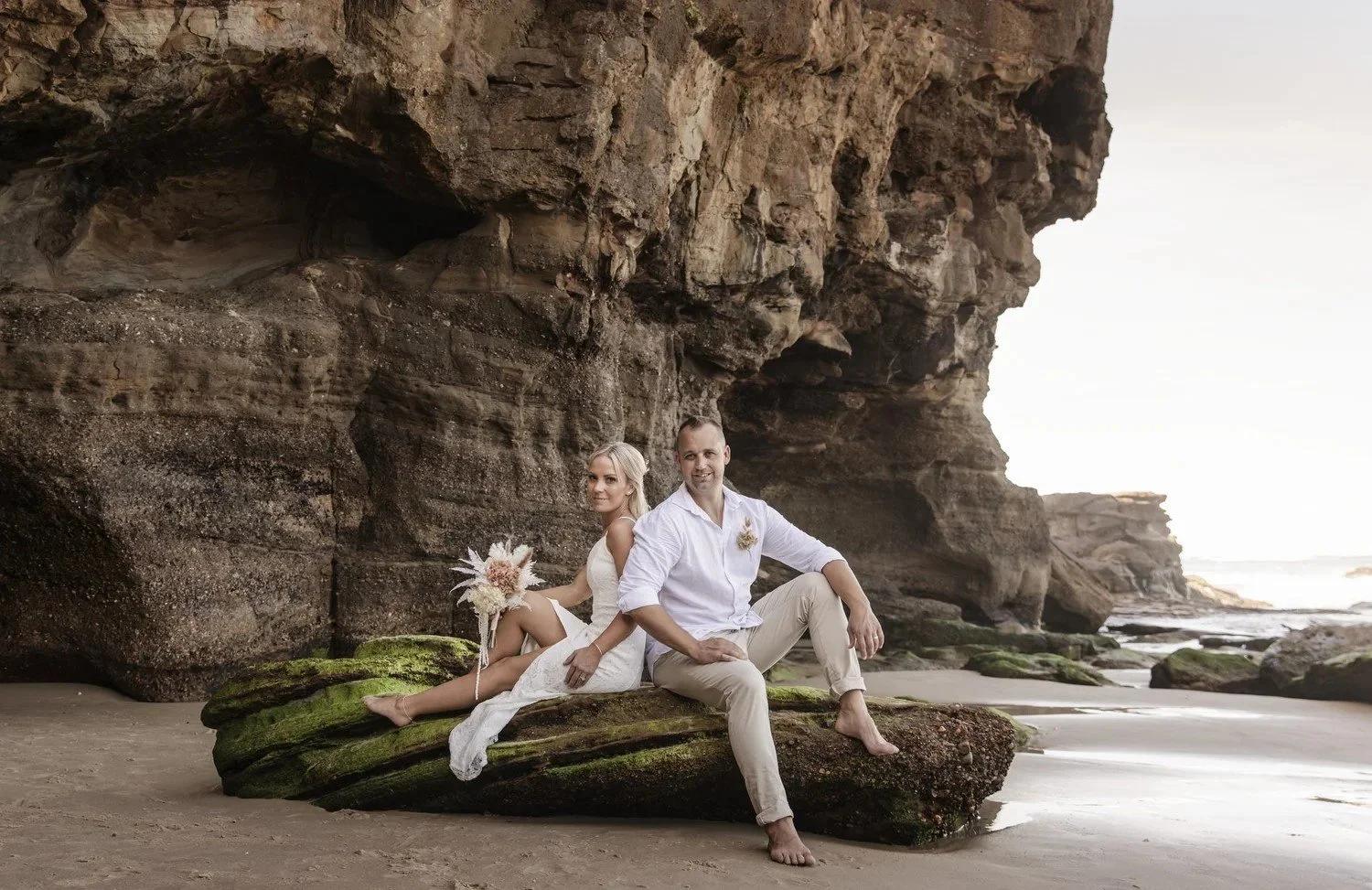 Couple lounging on a mossy rock at the entrance to a sea cave