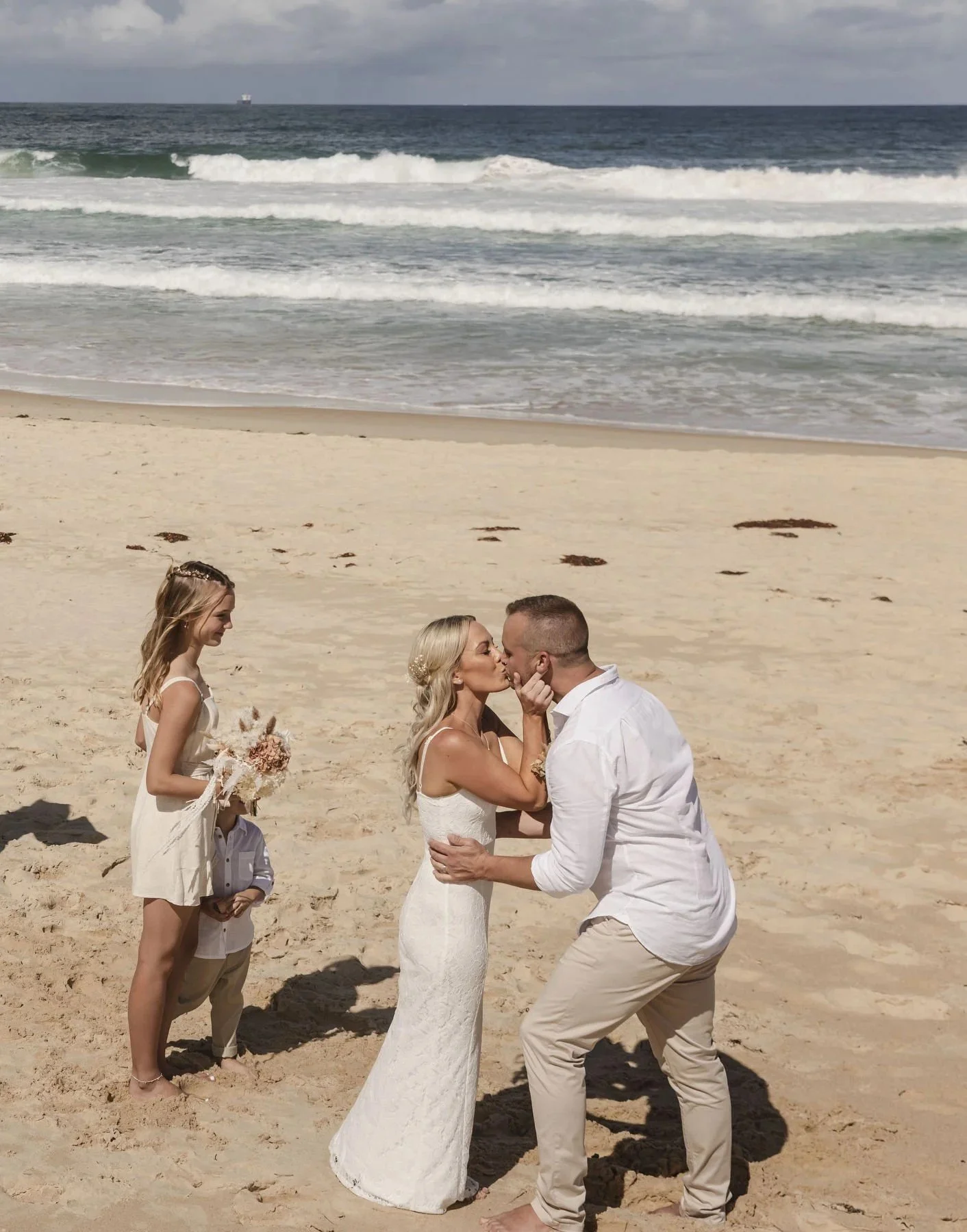 Couple kissing during their beach ceremony with the ocean behind