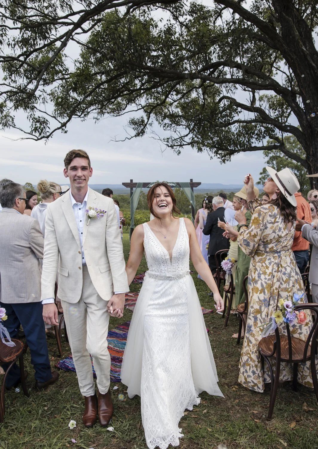 A bride and groom laughing as they walk hand in hand back down the aisle while guests cheer
