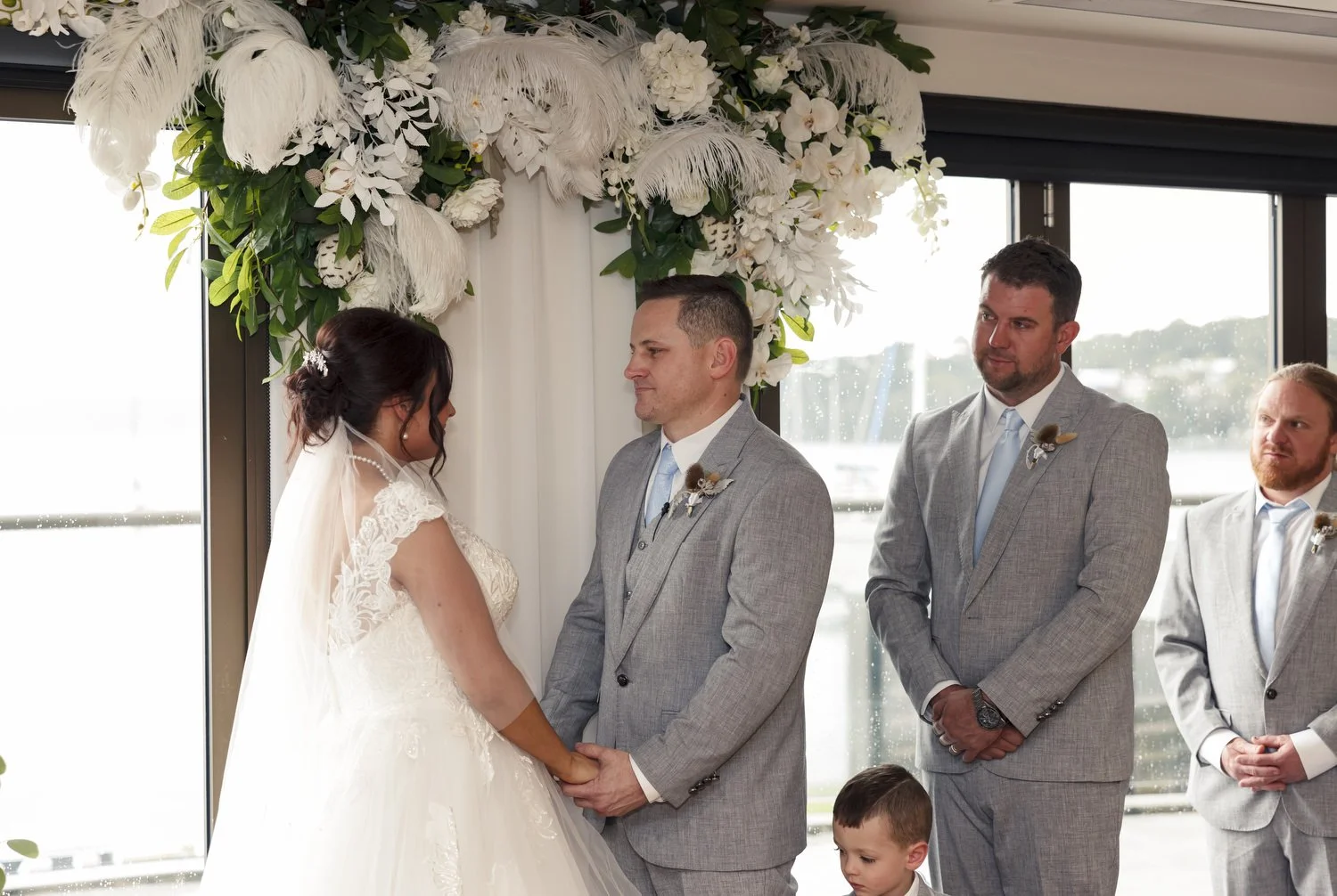 Wedding vows under a white floral arch by waterfront windows, Lake Macquarie