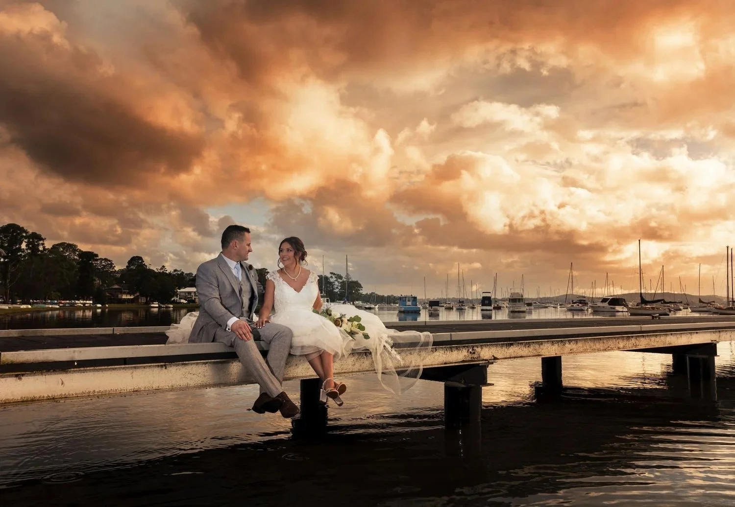 Couple sitting on a lakeside jetty under a golden sunset sky on Lake Macquarie