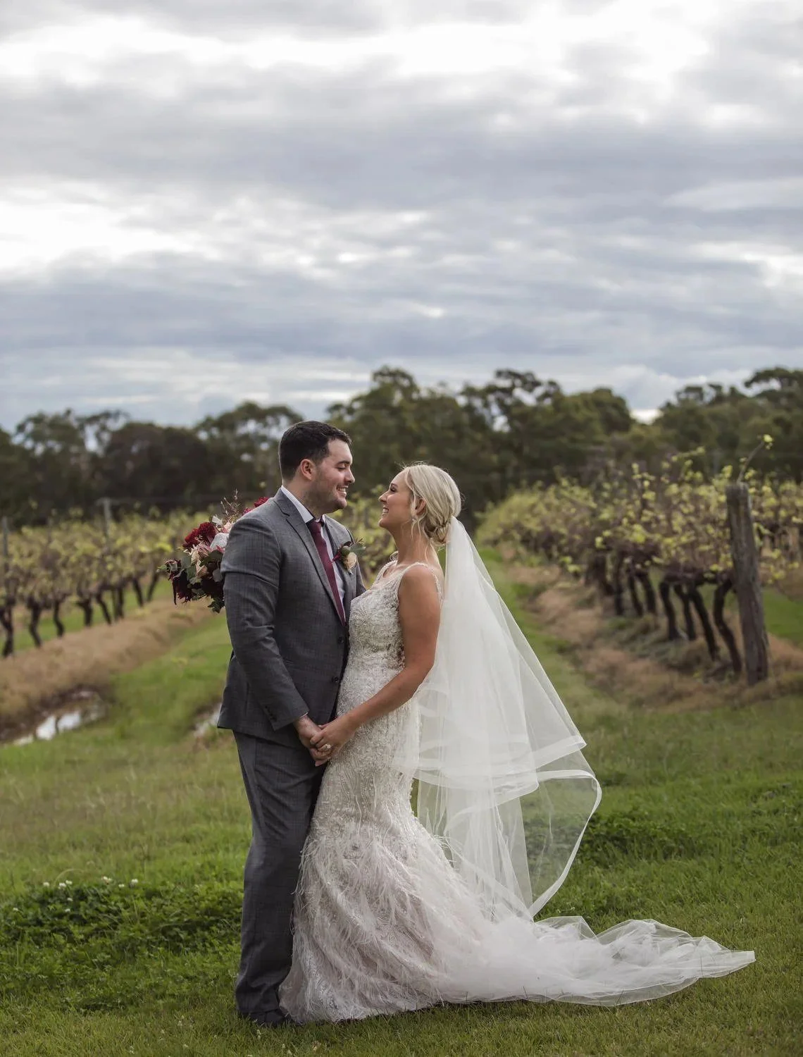 A couple facing each other and smiling among the grapevines under a cloudy sky