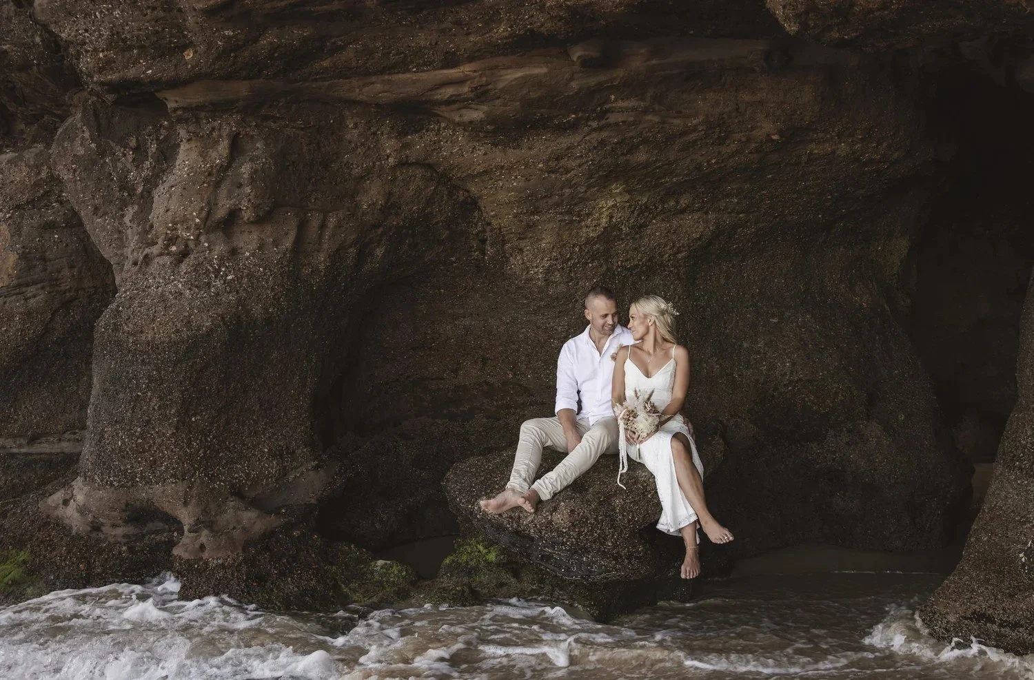 Couple sitting together inside a sandstone sea cave at Caves Beach