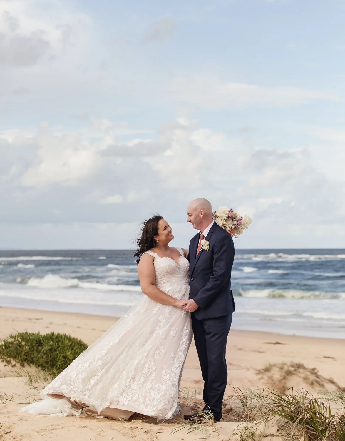 Bride and groom embracing on the beach as the waves roll in