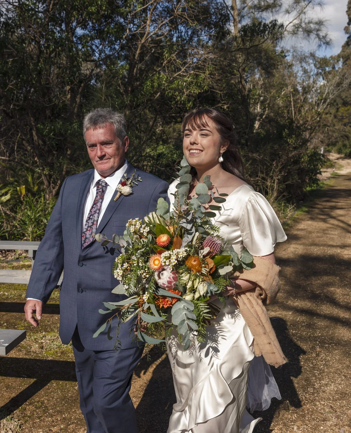 Bride laughing on her father’s arm with a bold native bouquet at a Newcastle wedding