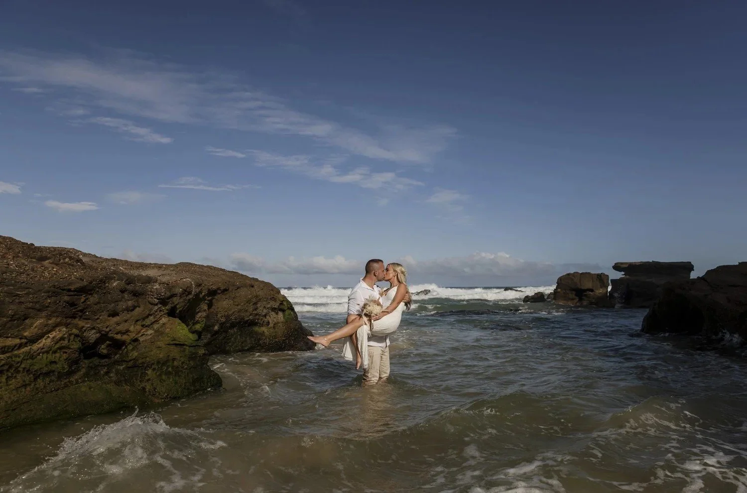 Family walking through shallow water between rocks at Caves Beach