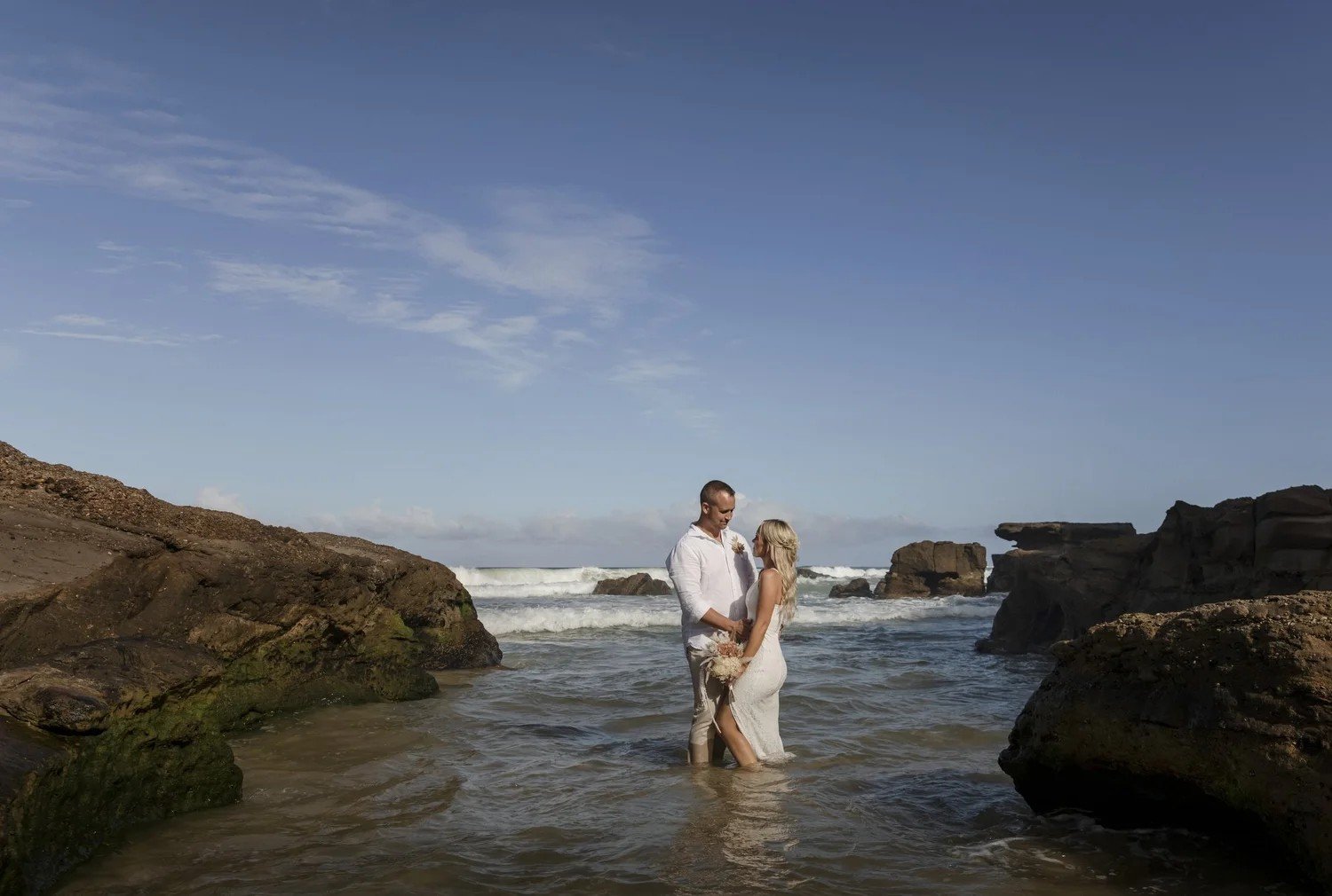 Couple standing in the shallows between rocks at Caves Beach