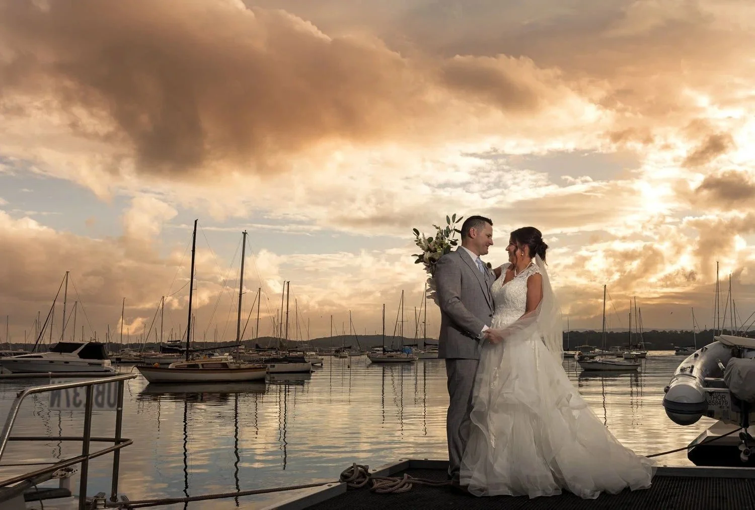 Bride and groom embracing on the foreshore at sunset with yachts on the lake