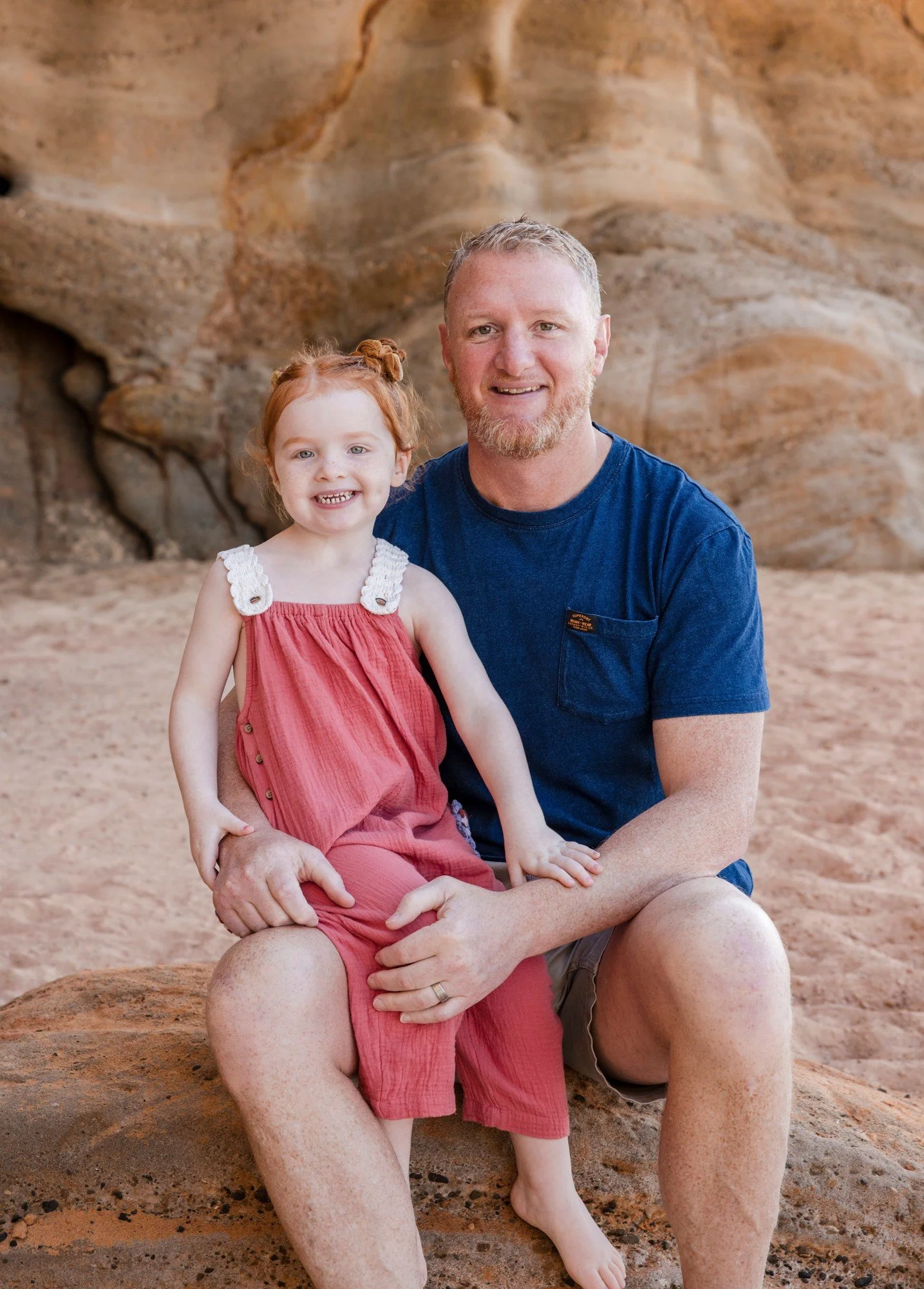 Dad sitting on a rock with his young daughter in a red dress beside him