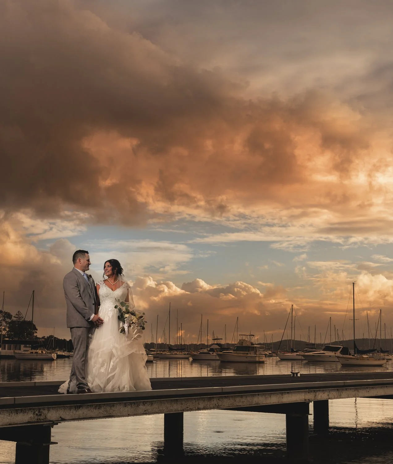 Couple on a jetty beneath a dramatic golden sunset sky on Lake Macquarie
