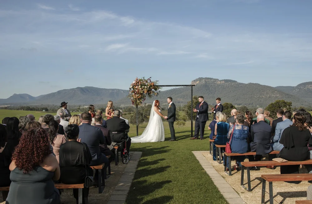 Guests on timber benches at a lawn ceremony with the Brokenback Range behind, Adams Peak Country Estate, Broke