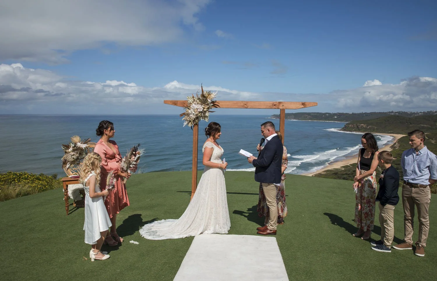Clifftop wedding ceremony under a timber arbour with the ocean and headland behind