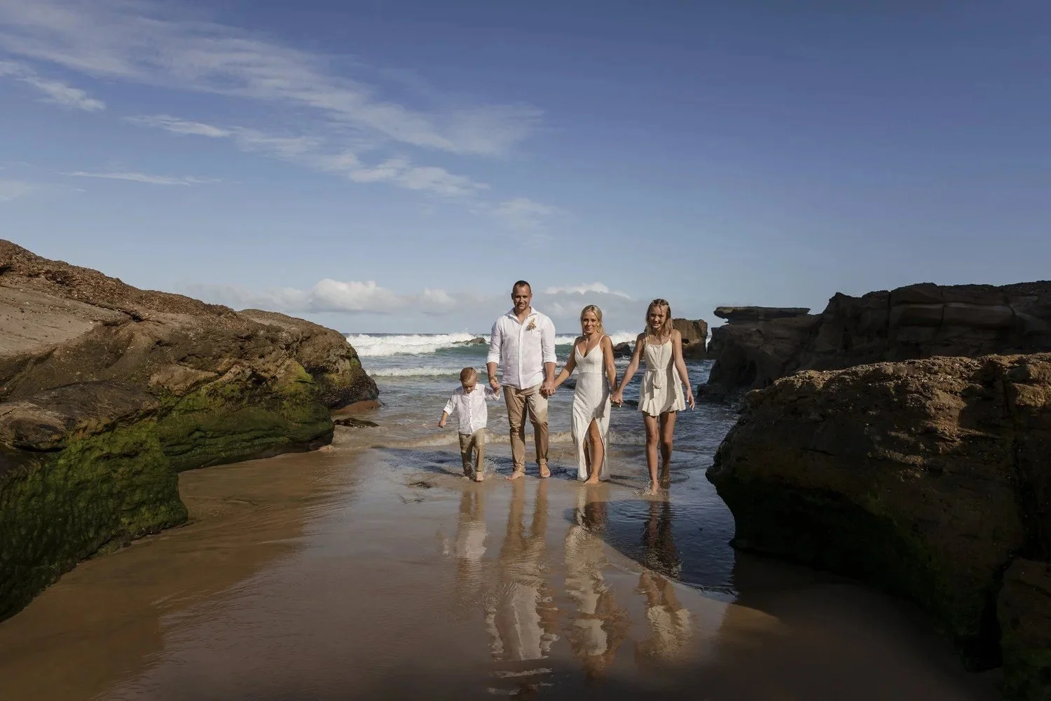 Family walking through shallow water between rocks at Caves Beach