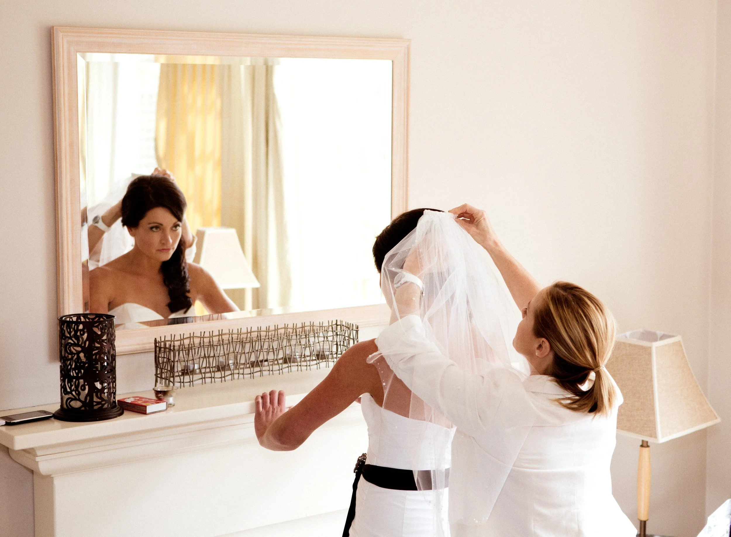 Bridesmaid fixing the bride's veil in front of a mirror while getting ready