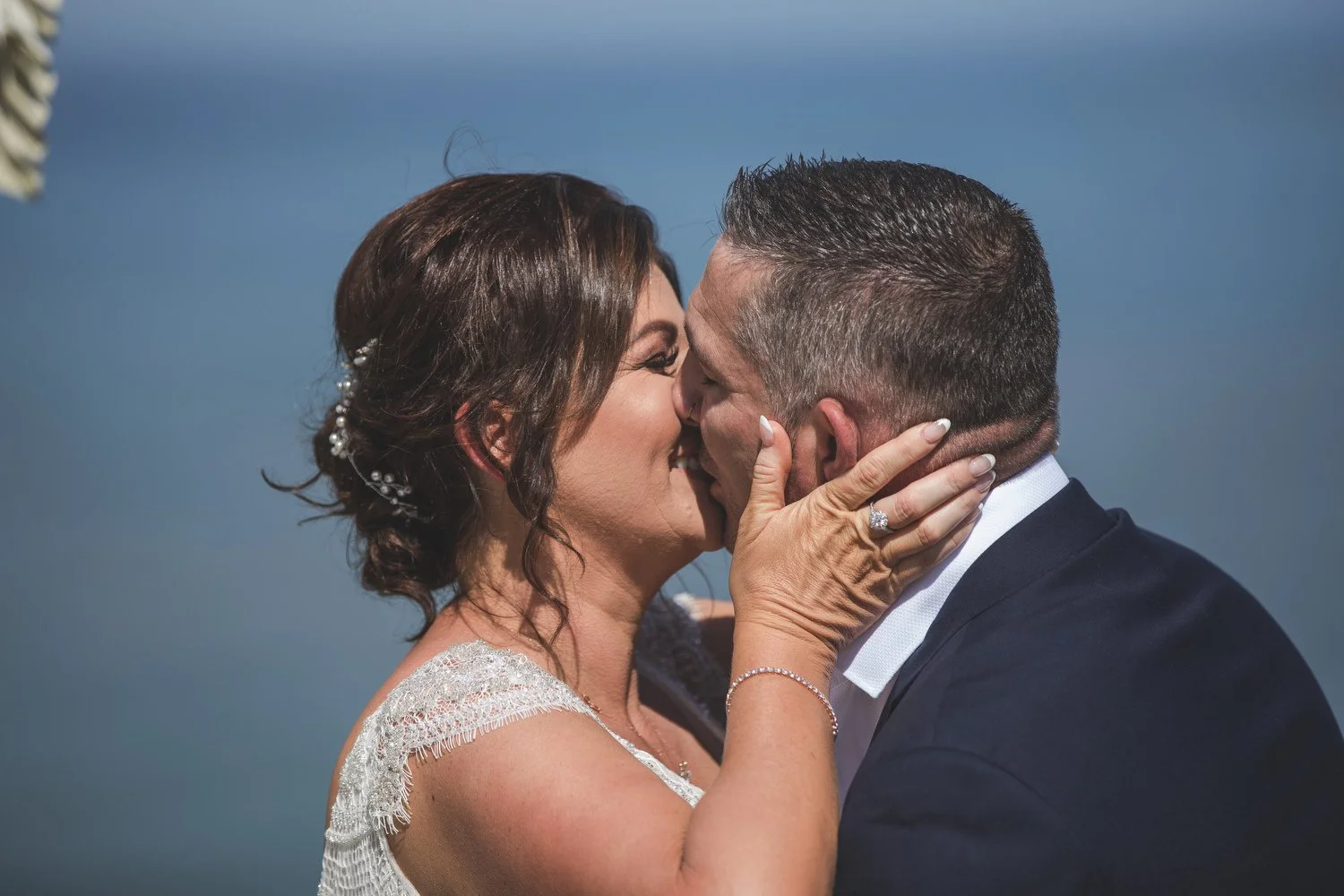 First kiss against a deep blue sky at a clifftop ceremony