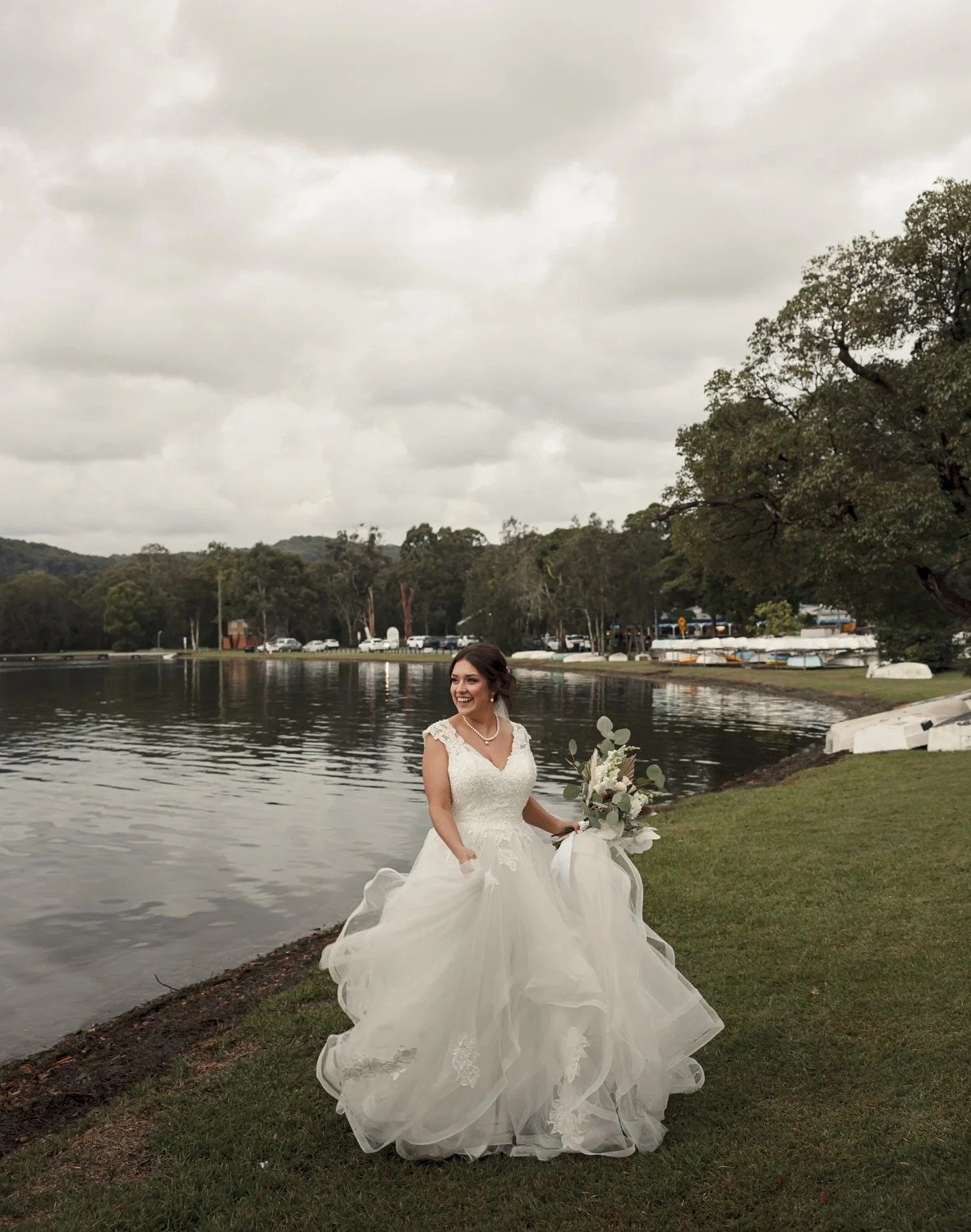 Bride standing on the grassy foreshore beside Lake Macquarie with moored boats behind