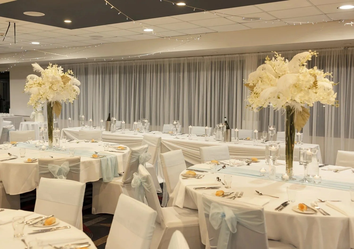 Function room at Valentine Bowling Club set with white linen and tall white floral centrepieces