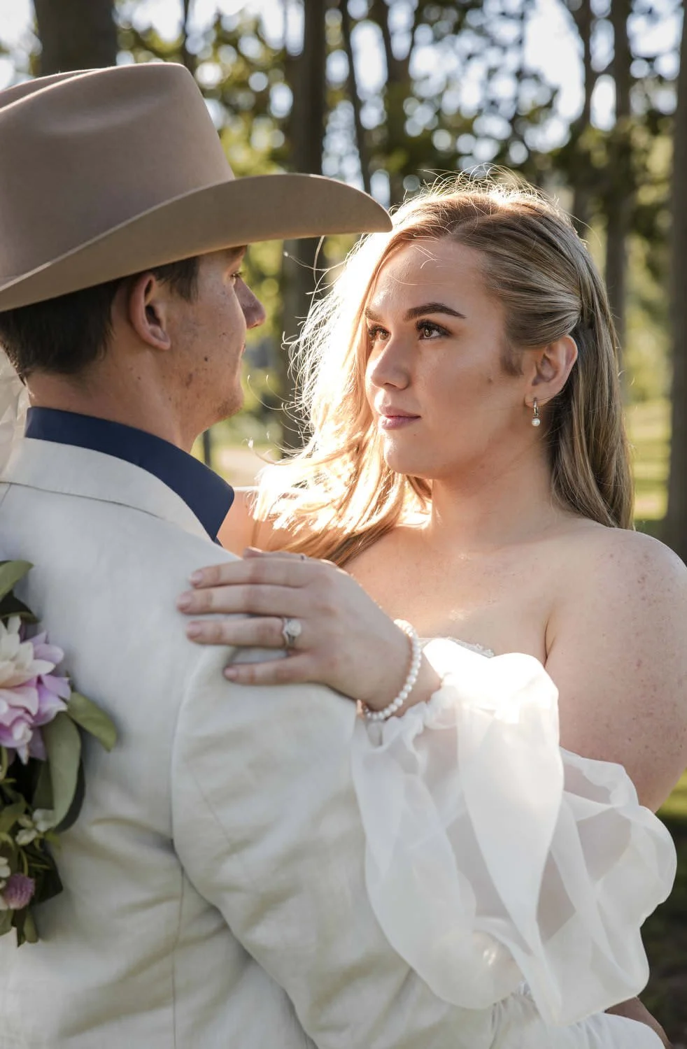 Groom in a wide-brimmed hat holding his bride close in soft late afternoon light