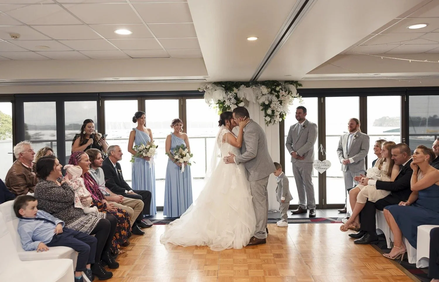 Indoor ceremony in front of lakeside windows with guests seated either side