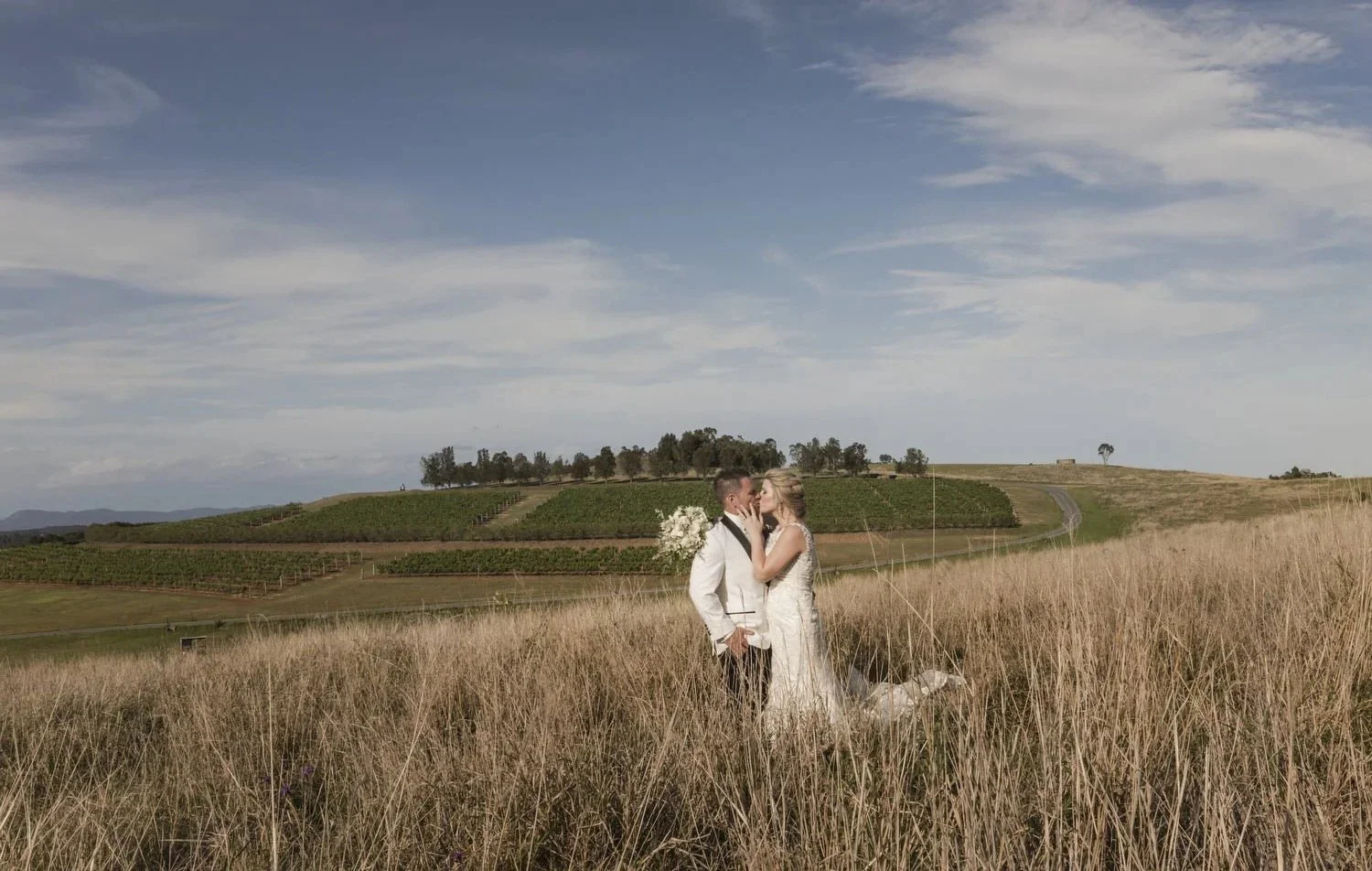 Couple in tall golden grass with rolling vineyard hills in the surrounding area, near Spicers Vineyards Estate, Pokolbin