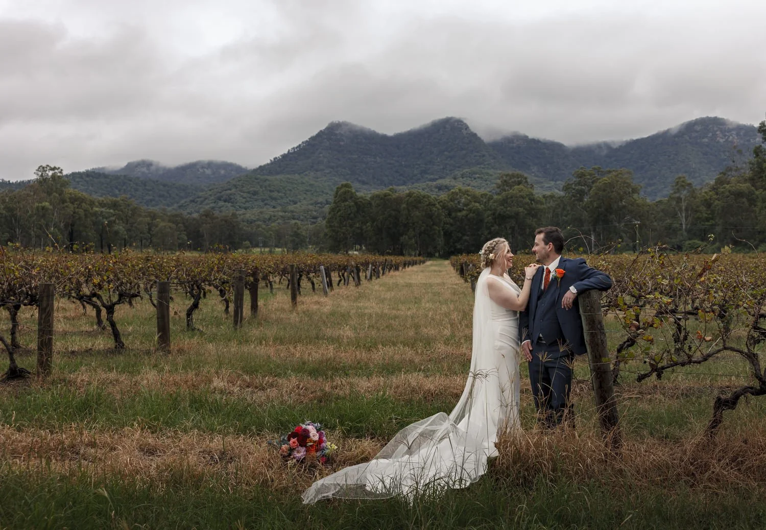 Couple standing in a vineyard with a misty mountain range behind